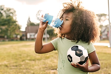 curly haired child holding soccer ball and drinking from water bottle