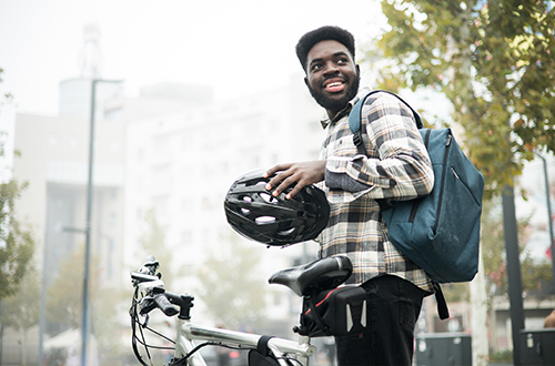 A Black man adjusts his helmet next to his e-bike