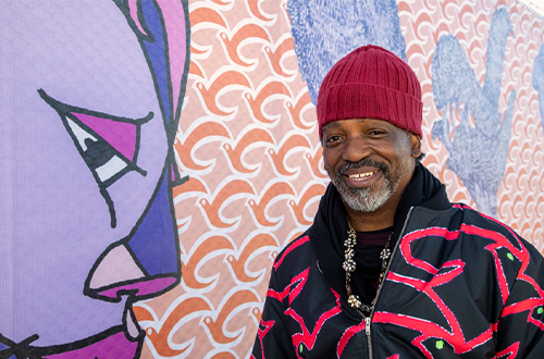 Bayview Hunters-Point native and artist Malik Seneferu standing in front of his mural