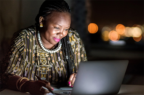 Una mujer negra y propietaria de un negocio trabaja en su computadora por la noche.