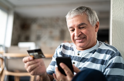 пожилой мужчина смотрит на смартфон и кредитную карту