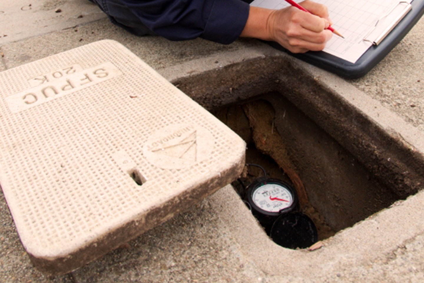 technician opening water meter cover on the sidewalk