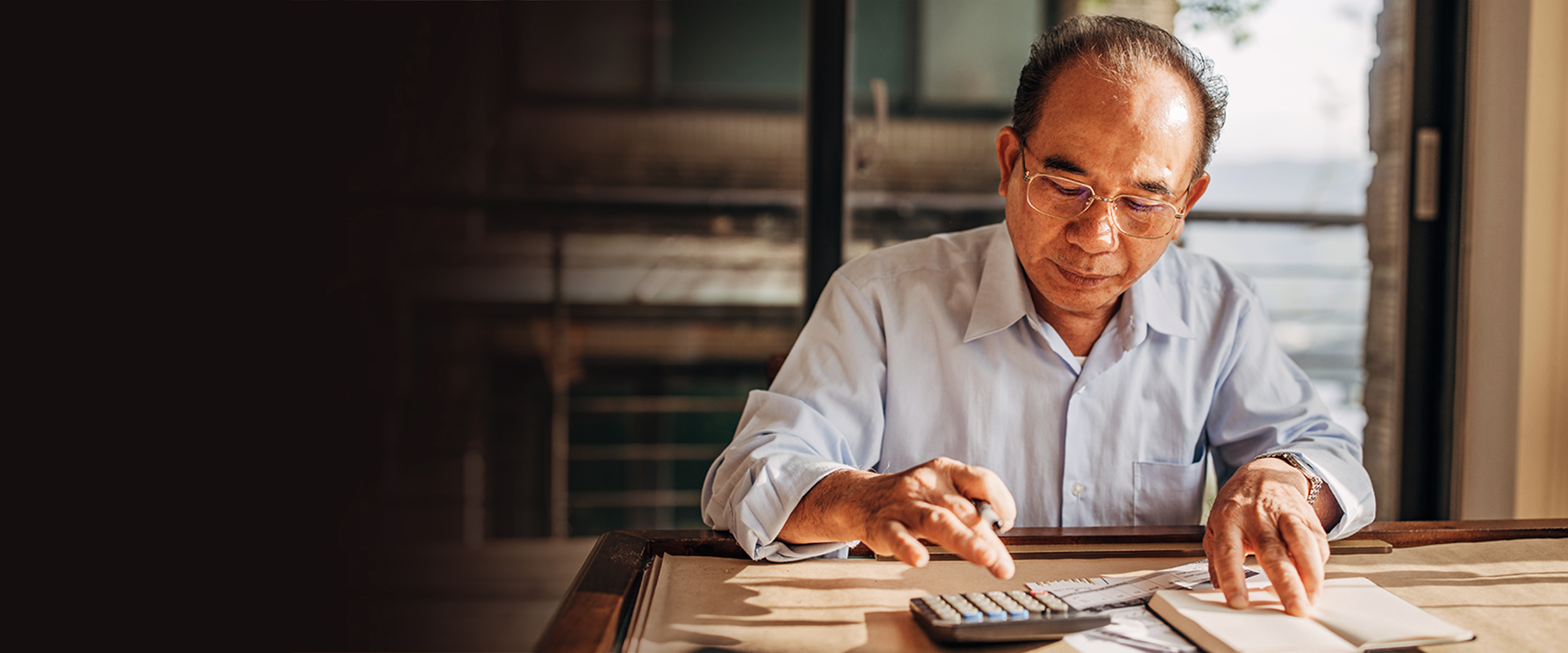 senior asian male at desk calculating a bill