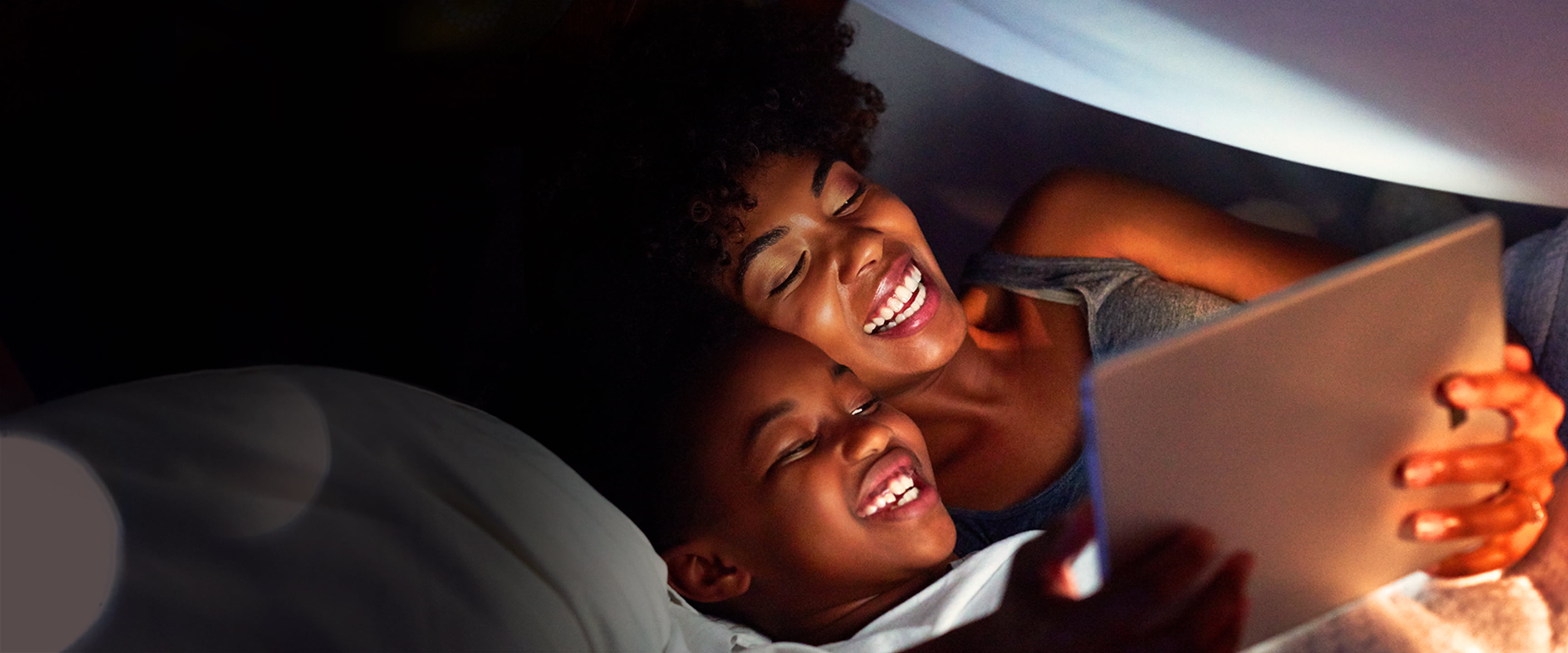 Mother and son reading a tablet in bed.