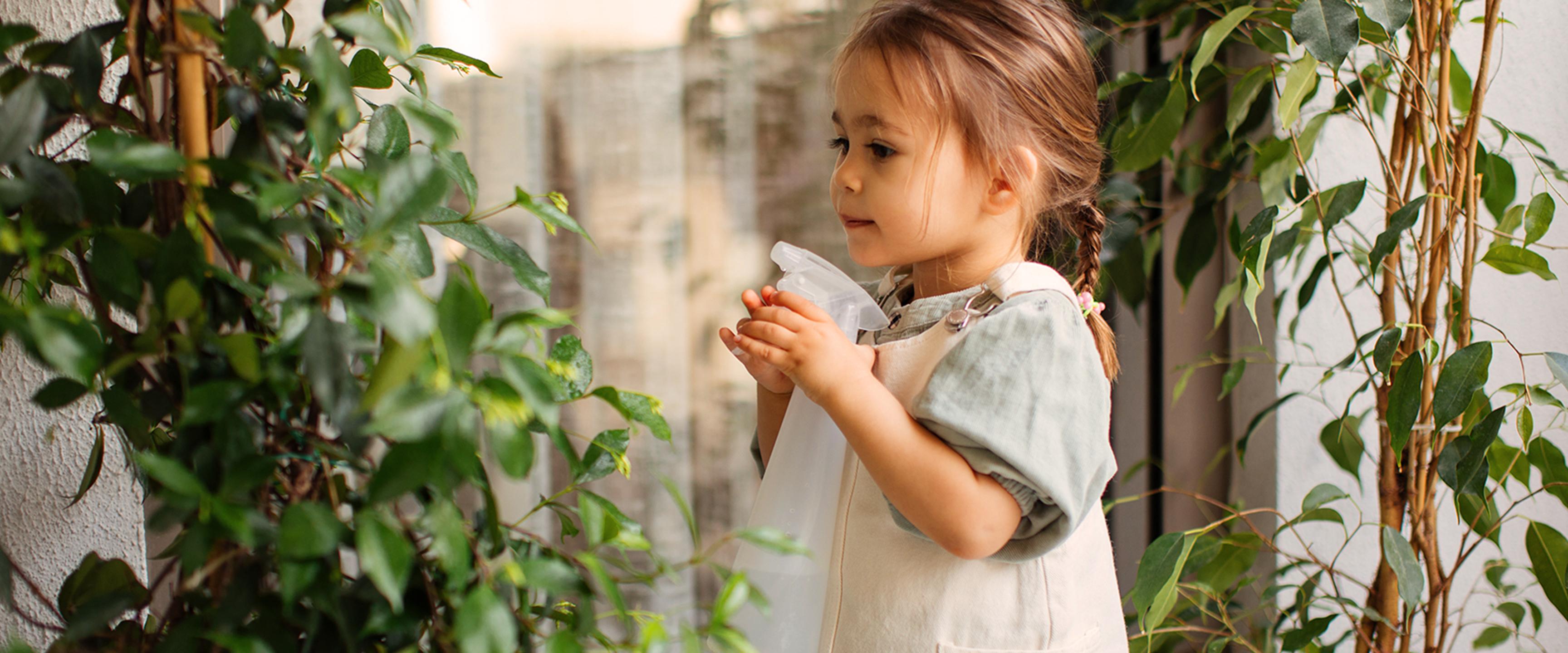 فتاة صغيرة تسقي النباتات بزجاجة رذاذ.