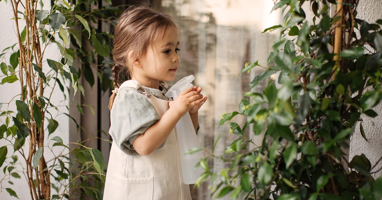 فتاة تحمل زجاجة رذاذ وتسقي نباتًا.