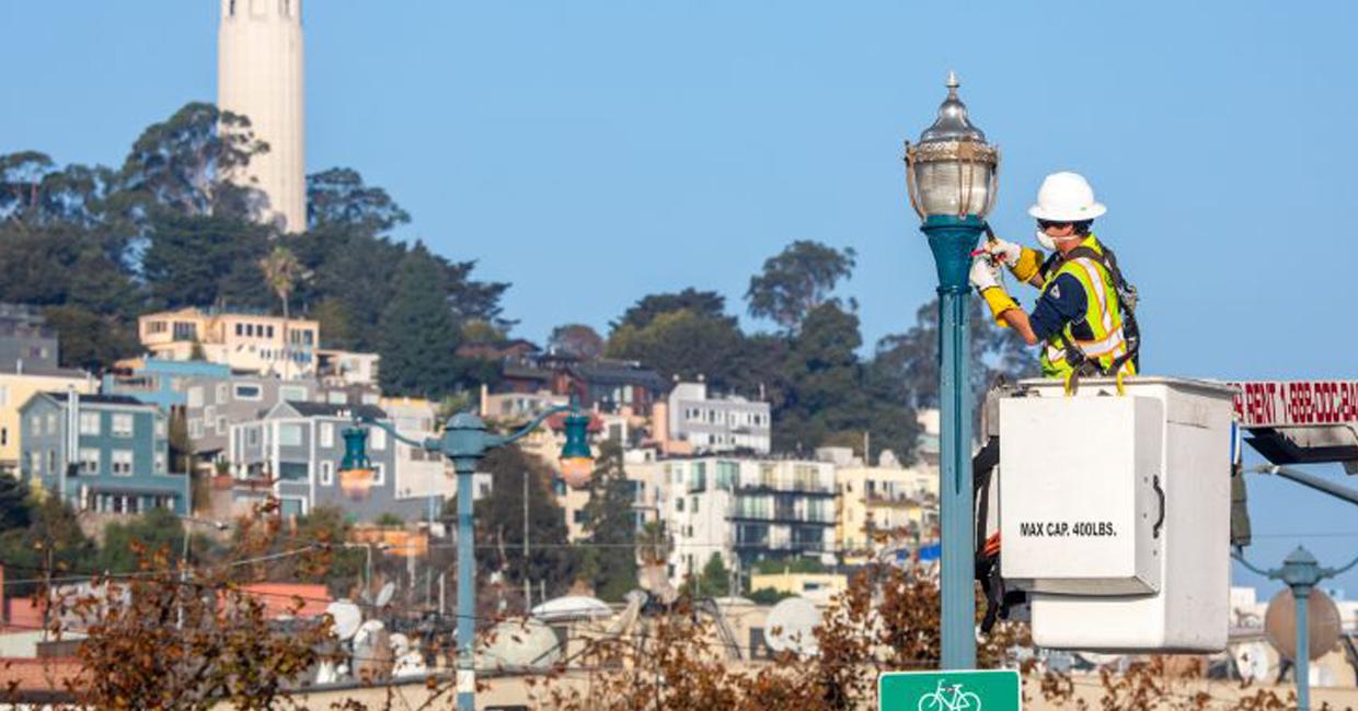 Рабочий SFPUC и фонарный столб на фоне Сан-Франциско