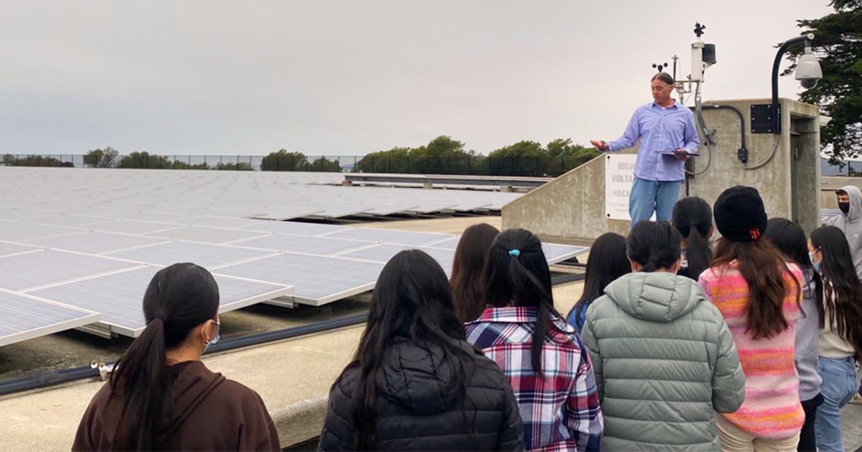 người đàn ông cho nhóm sinh viên xem một mảng năng lượng mặt trời lớn trên đỉnh hồ chứa
