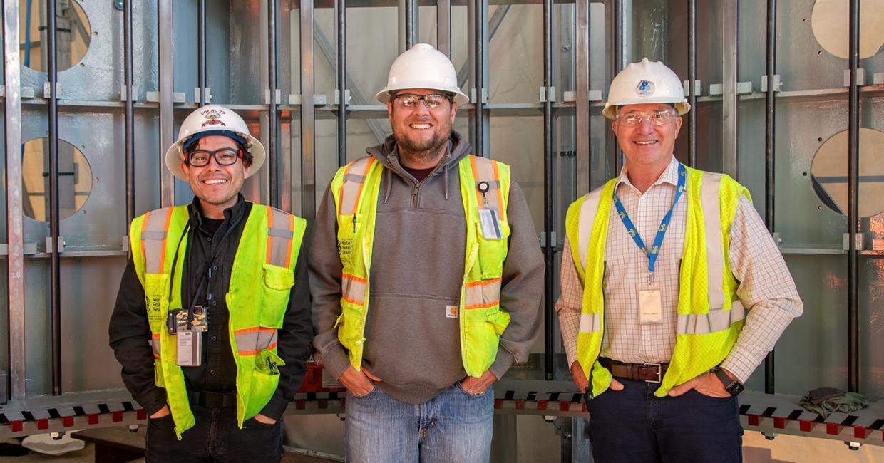 فريق إدارة البناء يقف داخل المولد الكهرومائي الجديد. من اليسار إلى اليمين: خوان باريوس (مهندس)، داستن شول (مهندس مقيم/متدرب تصميم طلابي في SFPUC)، تيم باركان (مدير المشروع).
