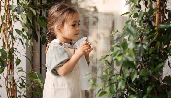 Chica sosteniendo una botella de spray y regando una planta.