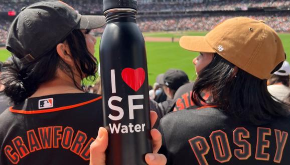 Dos fanáticos de los Gigantes de SF en un juego de béisbol y una botella de agua de SF en primer plano.