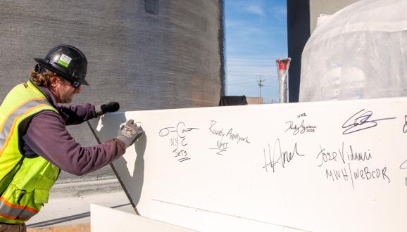 Will Crow, inspector del Equipo de Gestión de Construcción de la SFPUC, firma la viga de acero que será la viga más alta colocada en el Proyecto de Digestores de Biosólidos (BDFP).