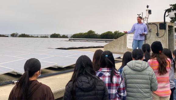 man showing group of students a large solar array on top of a reservoir